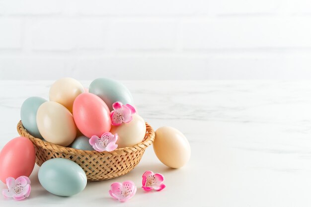 Sluit omhoog van kleurrijke paaseieren in de mand met roze pruimbloem op heldere witte houten lijstachtergrond.