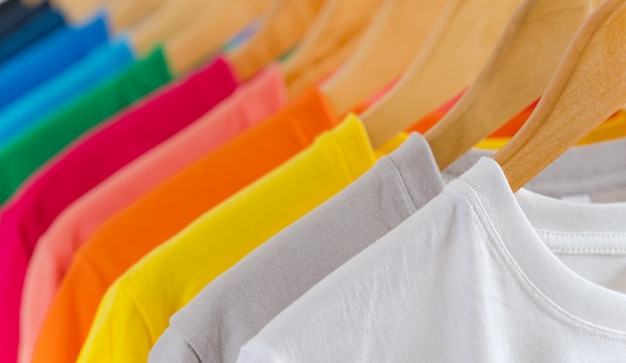 Sluit omhoog van Kleurrijke t-shirts op hangers, kledingsachtergrond