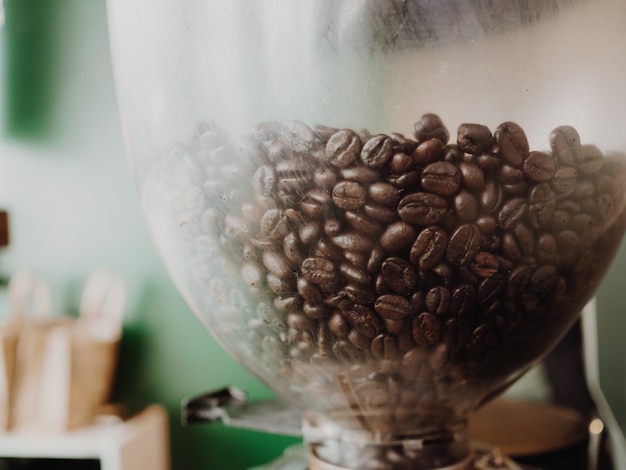 Sluit omhoog van koffiebonen in de machine met groene muur als achtergrond.