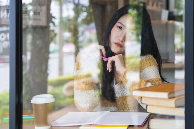 Foto sluit omhoog van mooie gele sweater dragen en student die terwijl het schrijven op notitieboekje glimlachen