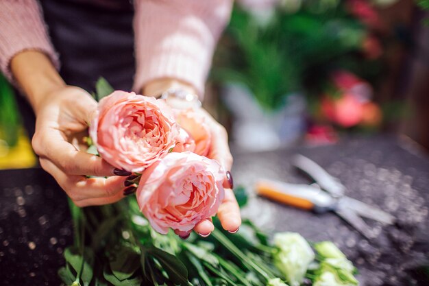 Sluit omhoog van mooie sinaasappel met de roze in hand greep van de rozenvrouw. Schaar en groene planten staan achter bloemen.