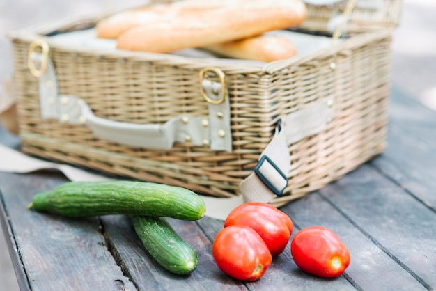 Sluit omhoog van tomaten en komkommers over houten lijst voor een open picknickmand.