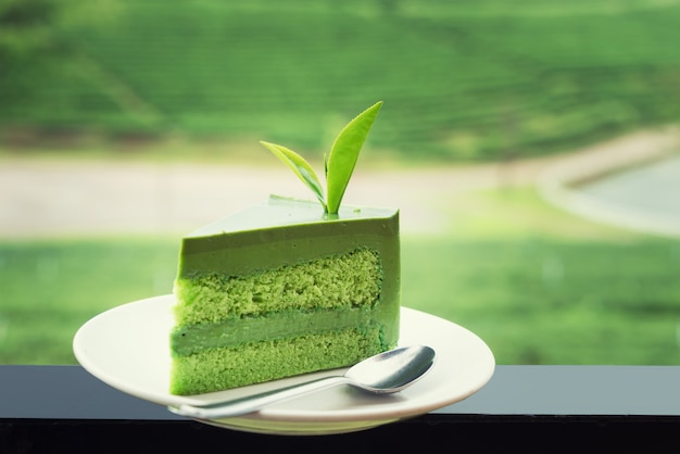 Sluit omhoog van verse groene theecake op witte plaat met theeaanplanting op achtergrond.