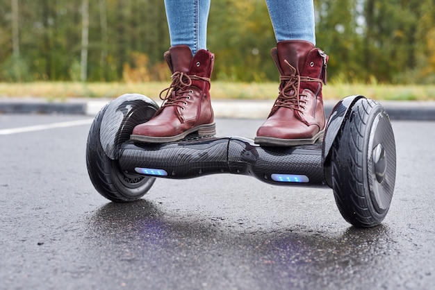 Sluit omhoog van vrouw gebruikend hoverboard op asfaltweg. Voeten op elektrische scooter buiten