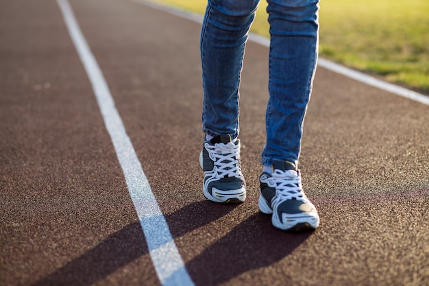 Sluit omhoog van vrouwenvoeten in sporttennisschoenen en jeans bij het run van steeg op buitensportenhof.