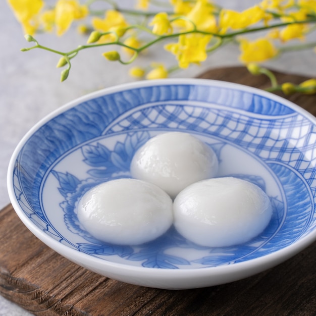 Sluit omhoog van yuanxiao tangyuan (kleverige rijstbolballen) in een kom op grijze lijst met bloem, voedsel voor Chinees Lantaarn Yuanxiao Festival.