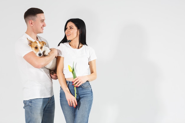 Sluit portret omhoog jong paar met gele bloemen en hond. mooi paar omarmen met dromerige amoureuze uitdrukking. Gelukkig hondenleven. Liefdevolle familie. Vrouwendag vieren.