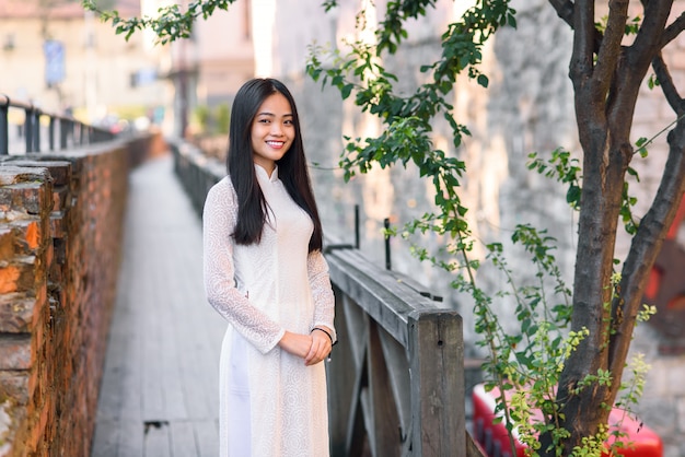 Sluit portret van mooie Aziatische vrouw gekleed in witte de kleding van Ao Dai bevindt zich dichtbij de boom op houten brug.