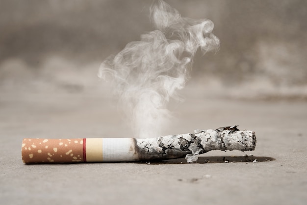 Sluit sigaret omhoog het branden op concrete vloer, einde met opheffend tabaksconcept