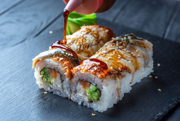 Sluit sushibroodje omhoog met roomkaas en paling. Sushi op steen donkere plaat op zwarte houten muur met kopie ruimte. Japans eten. giet teriyakisaus op sushi