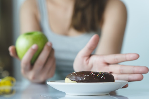 Sluit vrouw het gebruiken van hand omhoog met haar favoriete doughnut en kies groene appel.