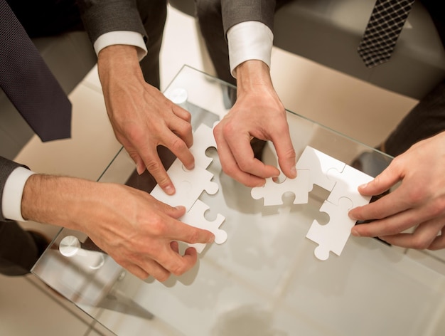 Sluit zakenmensen die een puzzel samenstellen achter een bureauhet concept van samenwerking