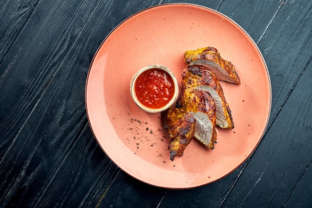 Smakelijk dieetgerecht - gegrilde kalkoenfilet op houtskool, geserveerd met rode saus in een bord op een donkere houten ondergrond. Turkije kebab