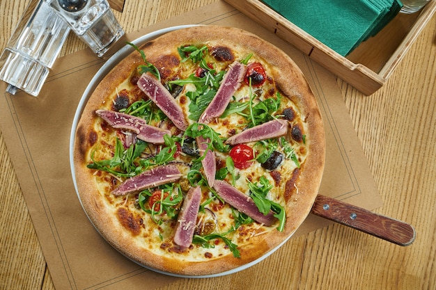 Smakelijk gebakken pizza met tonijn, rucola, cherrytomaatjes en parmezaanse kaas met knapperig op een houten tafel. Restaurant serveren. Pizza met zeevruchten. Bovenaanzicht