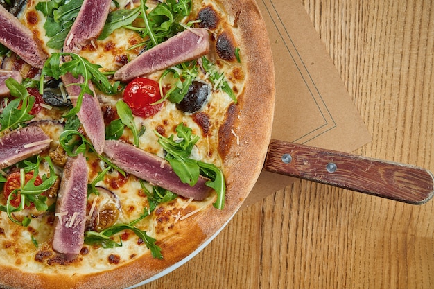 Smakelijk gebakken pizza met tonijn, rucola, cherrytomaatjes en parmezaanse kaas met knapperig op een houten tafel. Restaurant serveren. Pizza met zeevruchten. Bovenaanzicht