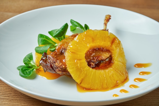 Smakelijk gekonfijte eendenbout met ananas en spinazie in een witte plaat op een houten tafel. Restaurant van de chef