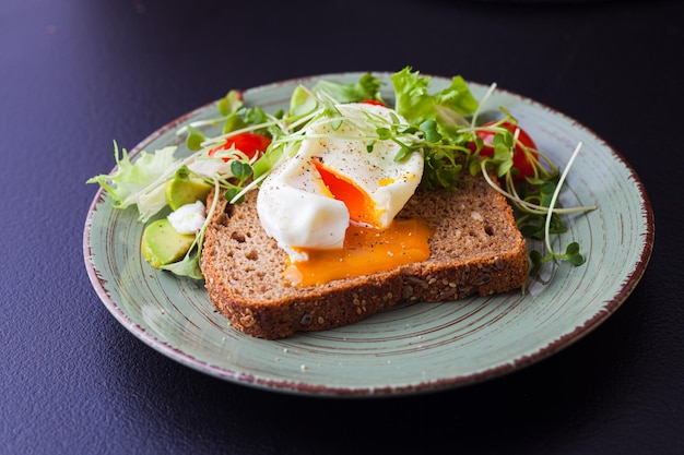 Smakelijk gekookt ei liggend op een sneetje roggebrood met verse salade rond Concept van gezond eten