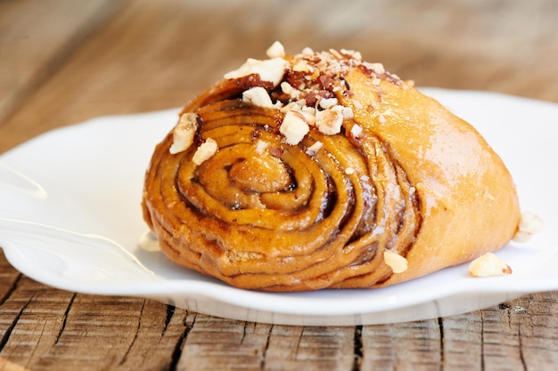 Smakelijk kaneelbroodje op een witte plaat. huisgemaakt gebak, broodje met noten topping