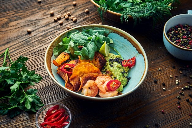 Smakelijk Mexicaans voorgerecht - avocado guacamole met garnalen, groente chips en koriander in een kom op een houten tafel. Close-up bekijken