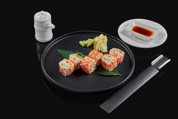 Smakelijk sushi california roll met tobik kaviaar, krab, avocado en komkommer op een zwarte keramische plaat op een zwarte ondergrond. japans traditioneel eten. foto voor het menu