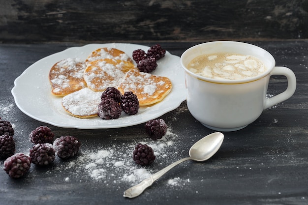 Foto smakelijke amerikaanse pannenkoeken met bramen, poedersuiker, koffie met marshmallow.