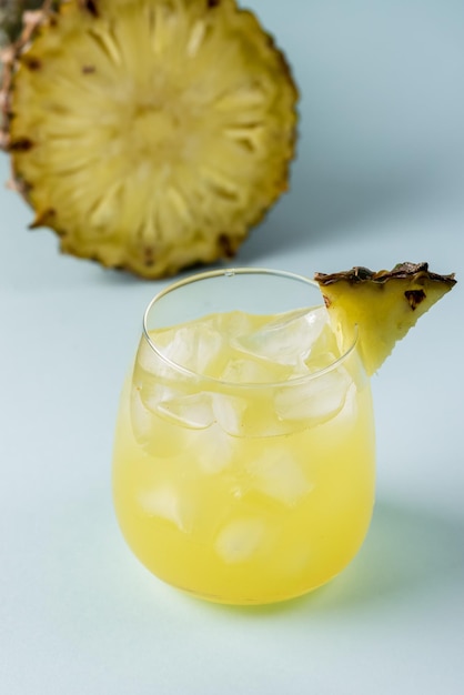 Smakelijke ananascocktail of sap in glas met ijsblokje gezonde drank blauwe achtergrond verticaal