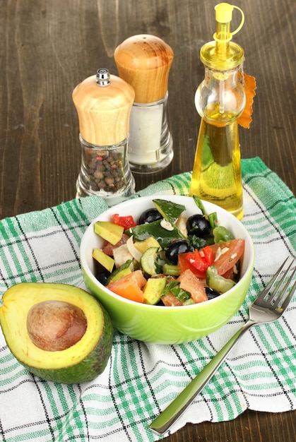 Smakelijke avocadosalade in kom omringd door kruiden op houten tafelclose-up