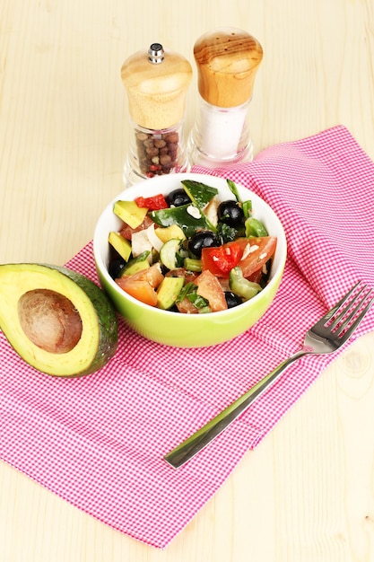 Smakelijke avocadosalade in kom omringd door kruiden op houten tafelclose-up