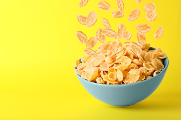 Smakelijke cornflakes die in kom vallen op gele ruimte als achtergrond voor tekst