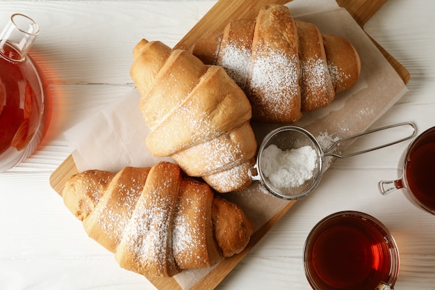 Smakelijke croissants en kopjes met thee op houten achtergrond, bovenaanzicht