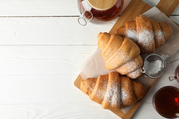 Smakelijke croissants en kopjes met thee op houten achtergrond, bovenaanzicht