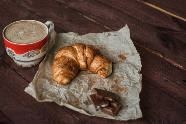 Smakelijke croissants met een kopje koffie en chocolade op houten tafel