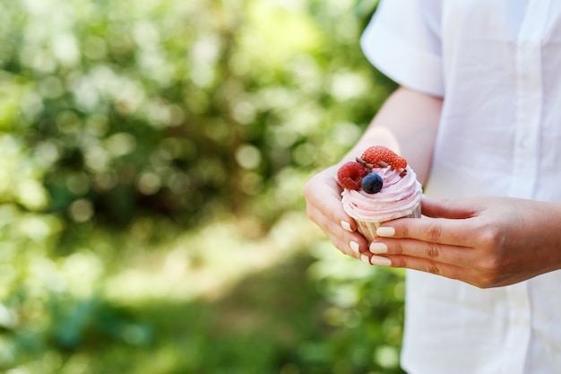 Smakelijke cupcake bedekt met roze room en zomerbessen in de handen van de vrouw. Groene bokeh