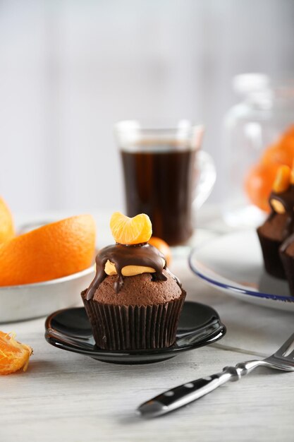 Smakelijke cupcake met plakje mandarijn en chocolade op een bord over lichte houten achtergrond