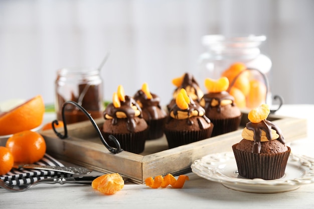 Smakelijke cupcakes met plakje mandarijn en chocolade op een dienblad over lichte houten achtergrond