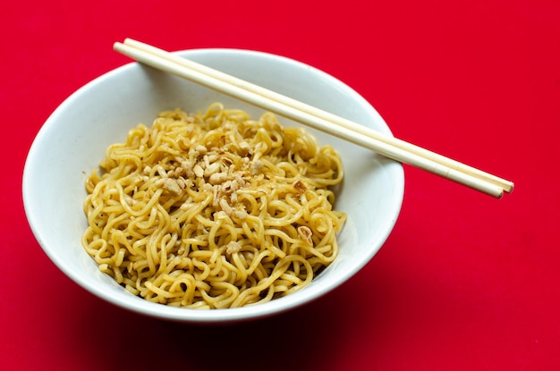 smakelijke gebakken instant noedels geserveerd op witte kom met houten chop stick geïsoleerd over rood.