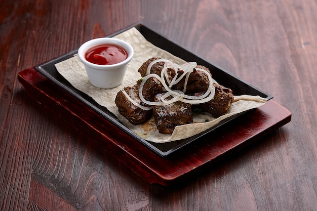 Smakelijke gegrilde vleesgerechten met saus op een donkere houten tafel.