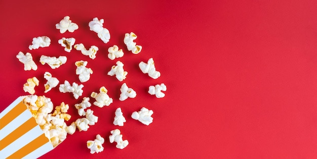 Smakelijke kaaspopcorn die uit een oranje gestreepte kartonnen emmer valt die op rode achtergrond wordt geïsoleerd