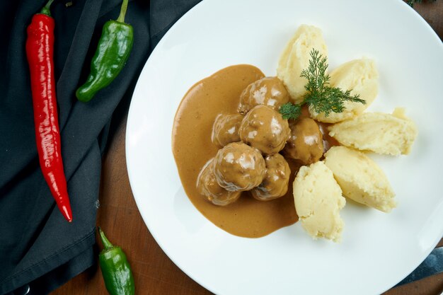 Smakelijke kipgehaktballetjes in saus met een bijgerecht van aardappelpuree in een witte plaat op een houten tafel in een compositie met ingrediënten