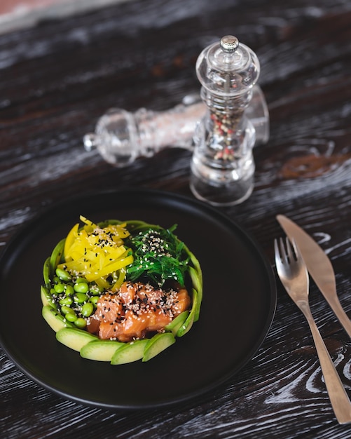 Smakelijke kom met zalm en groenten bestrooid met sesamzaadjes op een donkere achtergrond