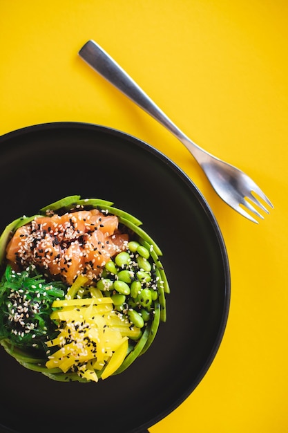 Smakelijke kom met zalm en groenten bestrooid met sesamzaadjes op een gele achtergrond