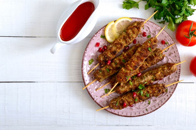 Smakelijke lula kebab op de plaat op een witte houten tafel. Gehakt vlees op houten spiesen, gegrild.