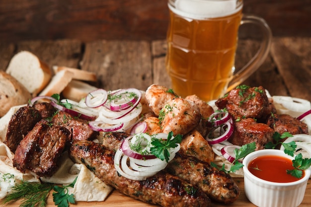 Smakelijke maaltijd in pub met vers gegrild vlees assortiment, pitabroodje, broodjes en mok koud licht bier geserveerd op houten oppervlak, close-up weergave.