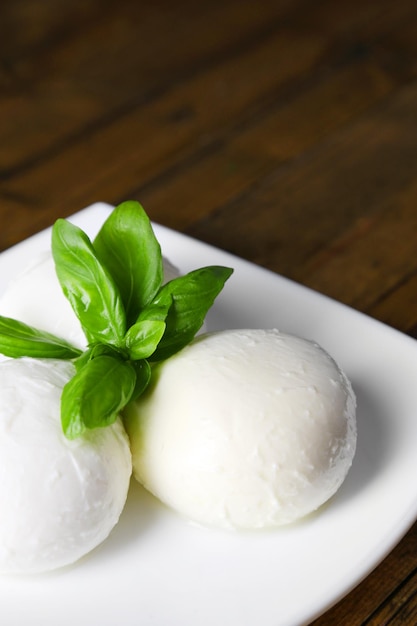 Smakelijke mozzarella kaas met basilicum op plaat op houten achtergrond