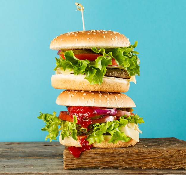 Smakelijke ongezonde hamburgers op houten bord op blauwe heldere achtergrond, klaar om te eten of te serveren. heldere achtergrond. selectieve focus.