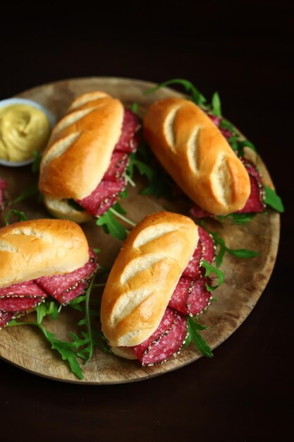 Smakelijke salamisandwiches met rucola en mosterd op een houten bord