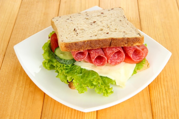 Smakelijke sandwich met salamiworst en groenten op witte plaat op houten ondergrond
