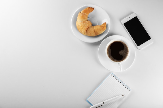 Smakelijke sikkelbroodje met kopje koffie en telefoon op witte ondergrond