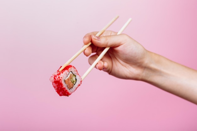 Smakelijke sushi roll Californië met houten stokjes op roze achtergrond close-up. Plaats voor bijschrift en tekst.