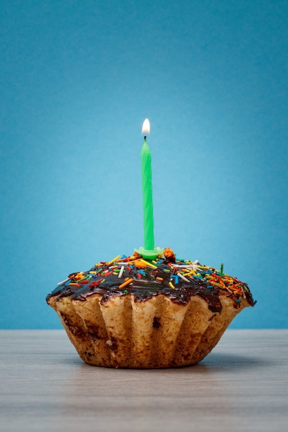 Smakelijke verjaardag cupcake met chocolade glazuur en karamel, versierd met feestelijke kaars branden op blauwe achtergrond. Gelukkige verjaardag minimaal concept.